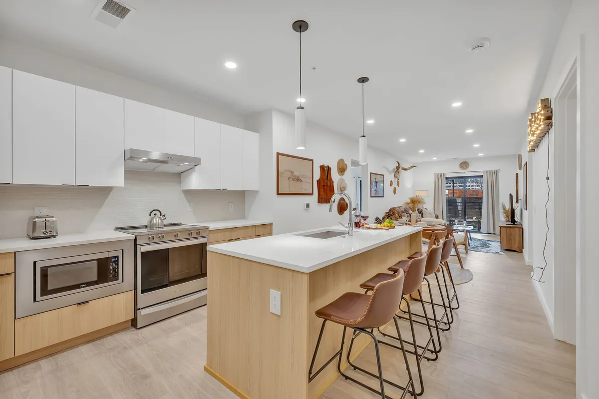 A bright kitchen featuring a large island with bar stools, stainless steel appliances, and decorative wall art. The open layout highlights the modern design and functionality of the kitchen, with the island and appliances clearly visible, ideal for cooking, entertaining, and casual dining.