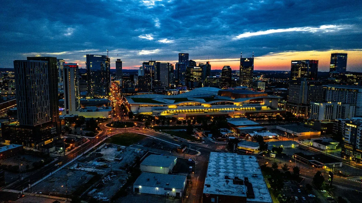 A sweeping view of Nashville's city skyline at sunset, illuminated by streetlights and glowing building facades. The scene evokes the city's dynamic nightlife and the electric energy that draws music lovers and explorers alike.
