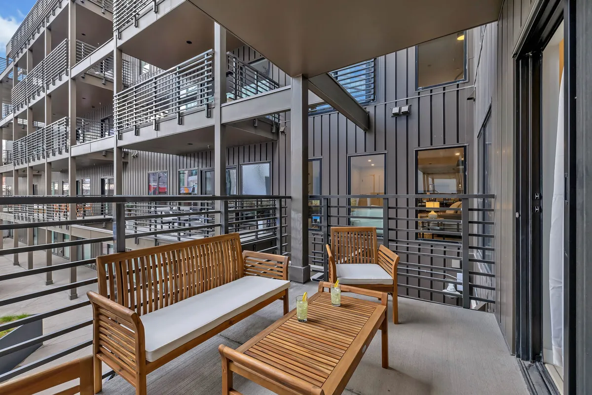 An inviting rooftop lounge with wooden seating and a coffee table, surrounded by railings that allow for elevated city views. The setting exudes a relaxed atmosphere ideal for socializing or unwinding after a busy day.
