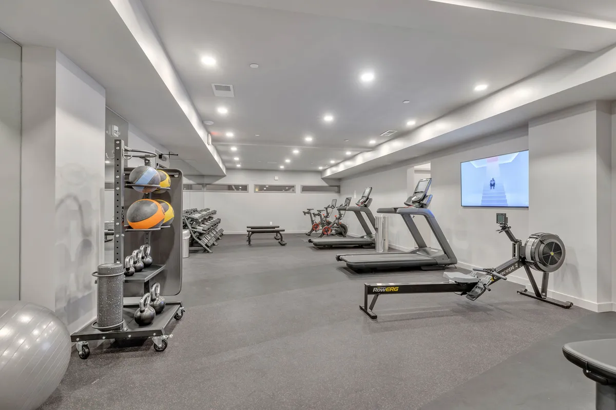 A bright, modern fitness center equipped with treadmills, stationary bikes, a rowing machine, kettlebells, and exercise balls. The space is open, motivational, and designed to foster both individual workouts and a sense of community among residents.