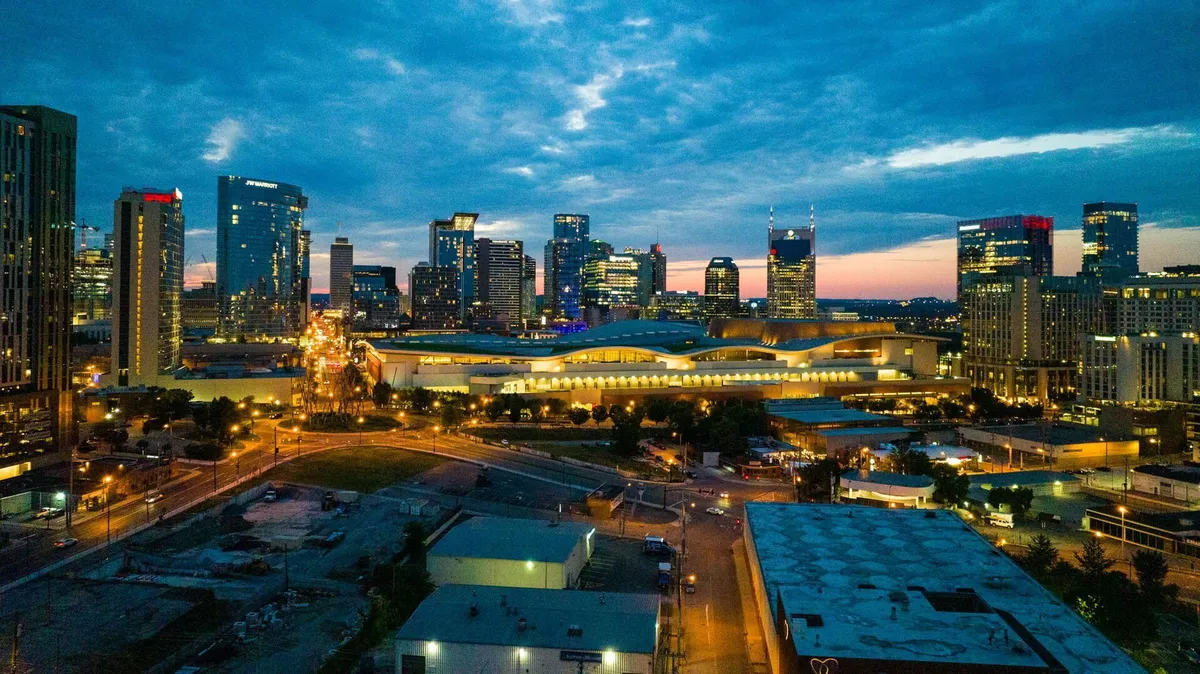 A sweeping city skyline at dusk, with illuminated buildings, lively streets below, and a glowing horizon. The overall mood is energetic and lively, inviting viewers to imagine exploring the city's vibrant nightlife and music venues.