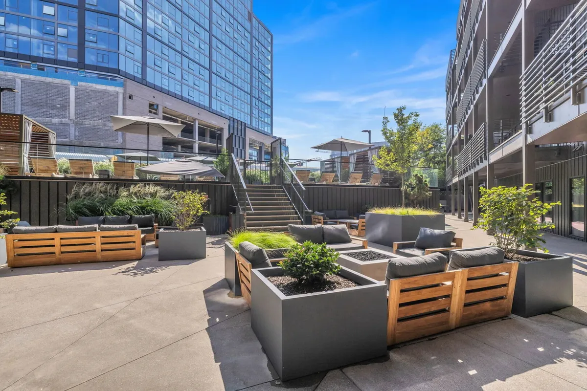 A welcoming rooftop lounge area showcasing modern lounge seating, planters with greenery, and a staircase leading to an upper-level escape. The setting suggests a relaxed atmosphere perfect for sunset views, group photos, and evening conversations.