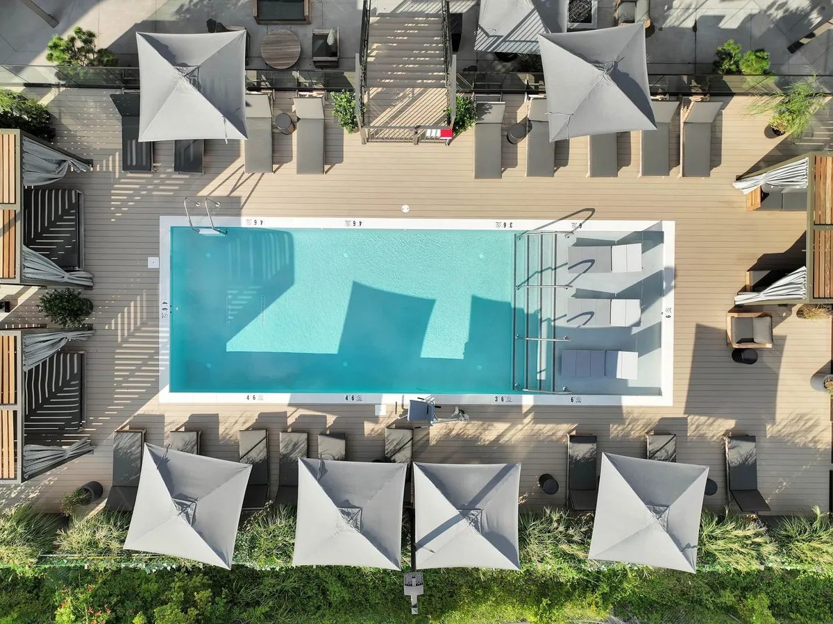 A vibrant pool area with clear blue water, surrounded by inviting lounge chairs and stylish cabana tents on a wooden deck. The space is set for relaxation and socializing, ideal for sunny afternoons or sunset gatherings.