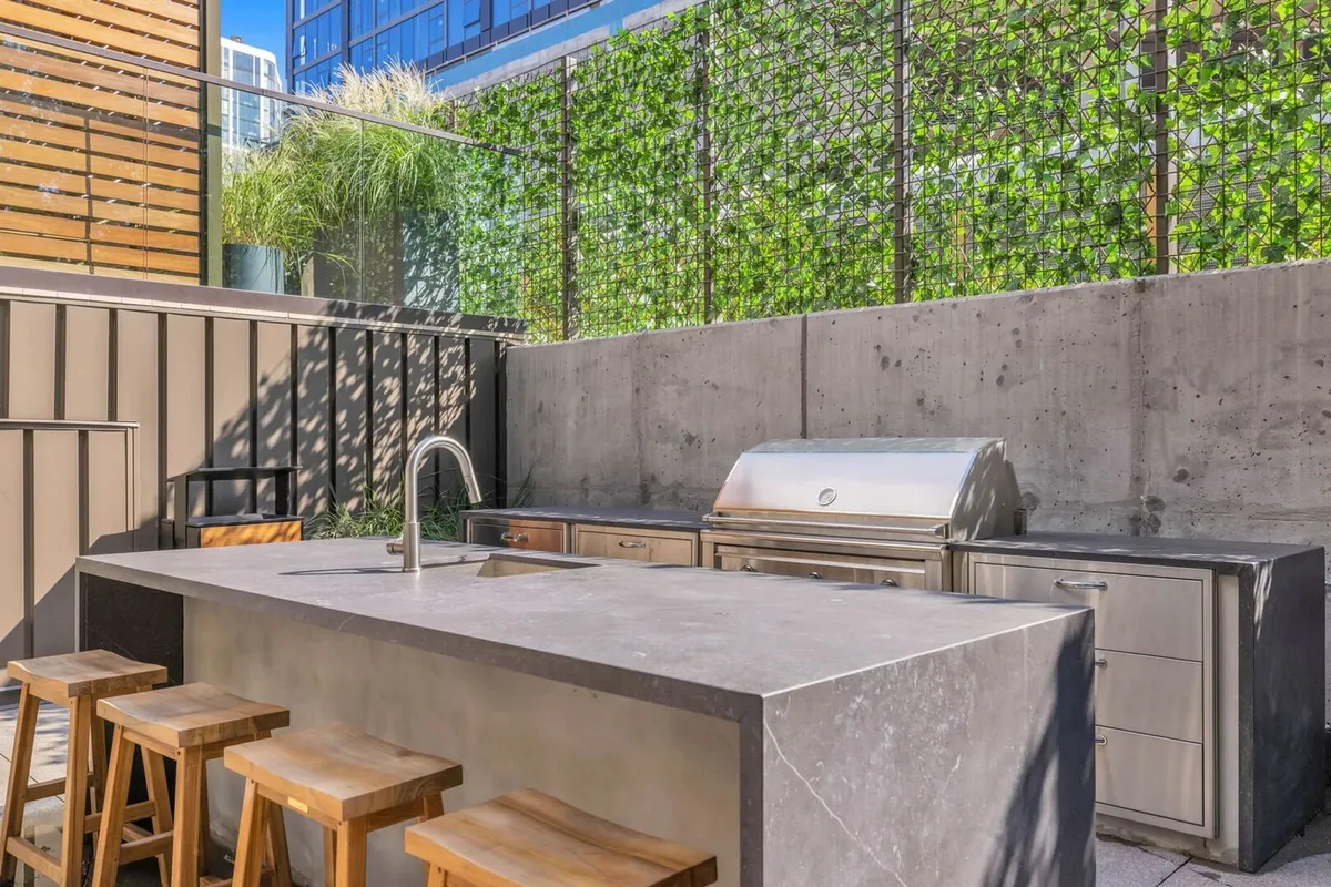 An outdoor kitchen area featuring a grill, stools, a green living wall, and a laid-back entertaining vibe. The space is designed for socializing, cooking, and enjoying meals outdoors, with ample room for group gatherings or casual barbecues.