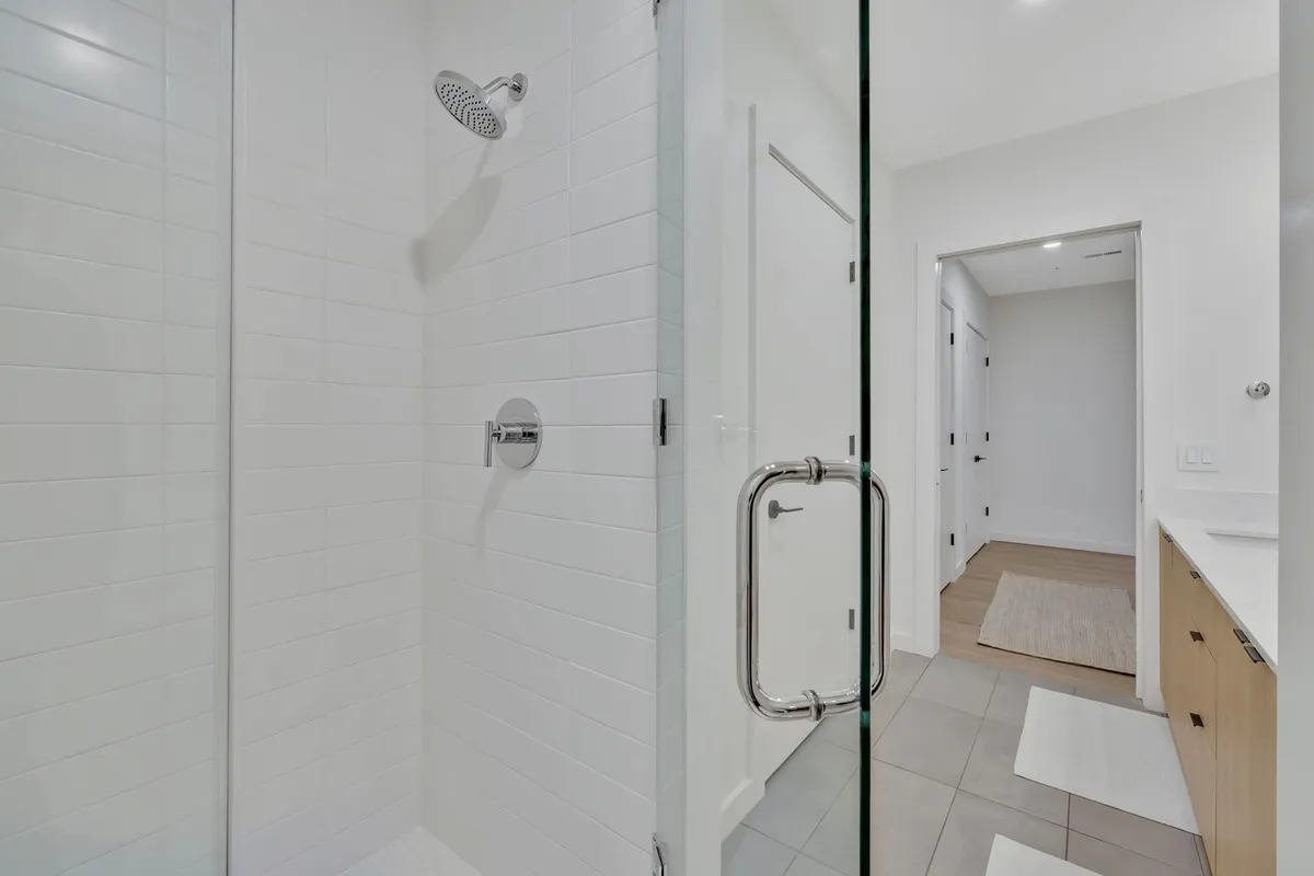 A modern bathroom with a glass shower enclosure, a sleek showerhead, and neutral tile flooring. The space is bright, fresh, and designed for comfort and rejuvenation, reflecting the upgraded bathroom amenities.