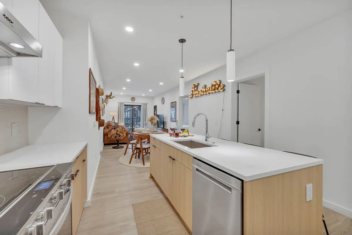 This image showcases a modern kitchen with a central island, stainless steel appliances, and an adjacent dining area. Decorative wall art and cozy lighting contribute to the inviting atmosphere. The kitchen island is set up for socializing with bar seating and the dining area is visible in the background, perfectly illustrating where group meals and gatherings happen.