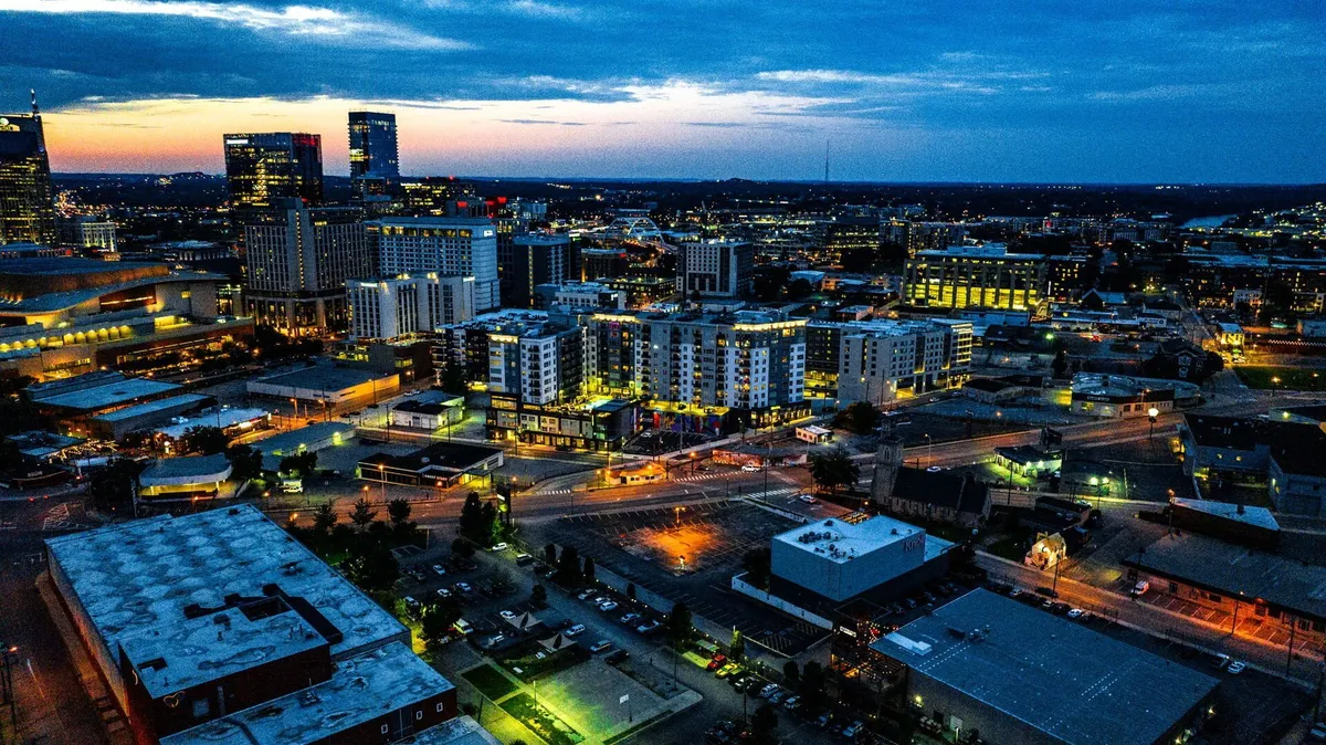 A panoramic view of the Nashville city skyline, illuminated buildings, and active streets with vibrant light trails at dusk. The image conveys the excitement and variety of downtown dining and nightlife.