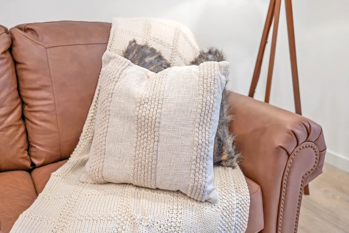 A living area with a brown leather couch, textured throw blanket, and decorative pillows, creating a cozy and inviting spot for relaxation or additional sleeping space with a pull-out sofa.