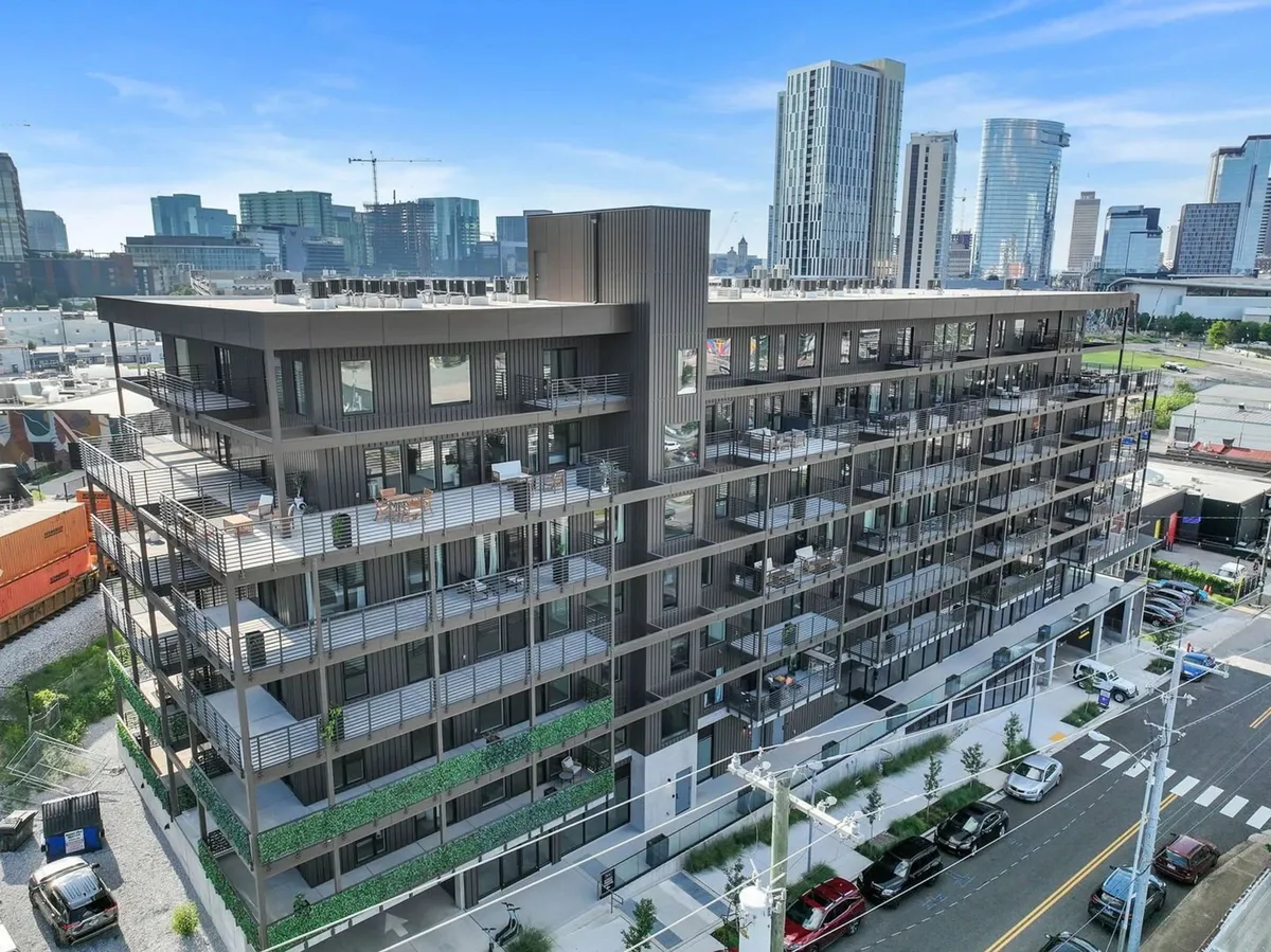 A contemporary apartment building with balconies overlooking the city skyline, set against a vibrant urban backdrop. The scene suggests urban living, social gatherings on balconies, and easy access to the heartbeat of Nashville.